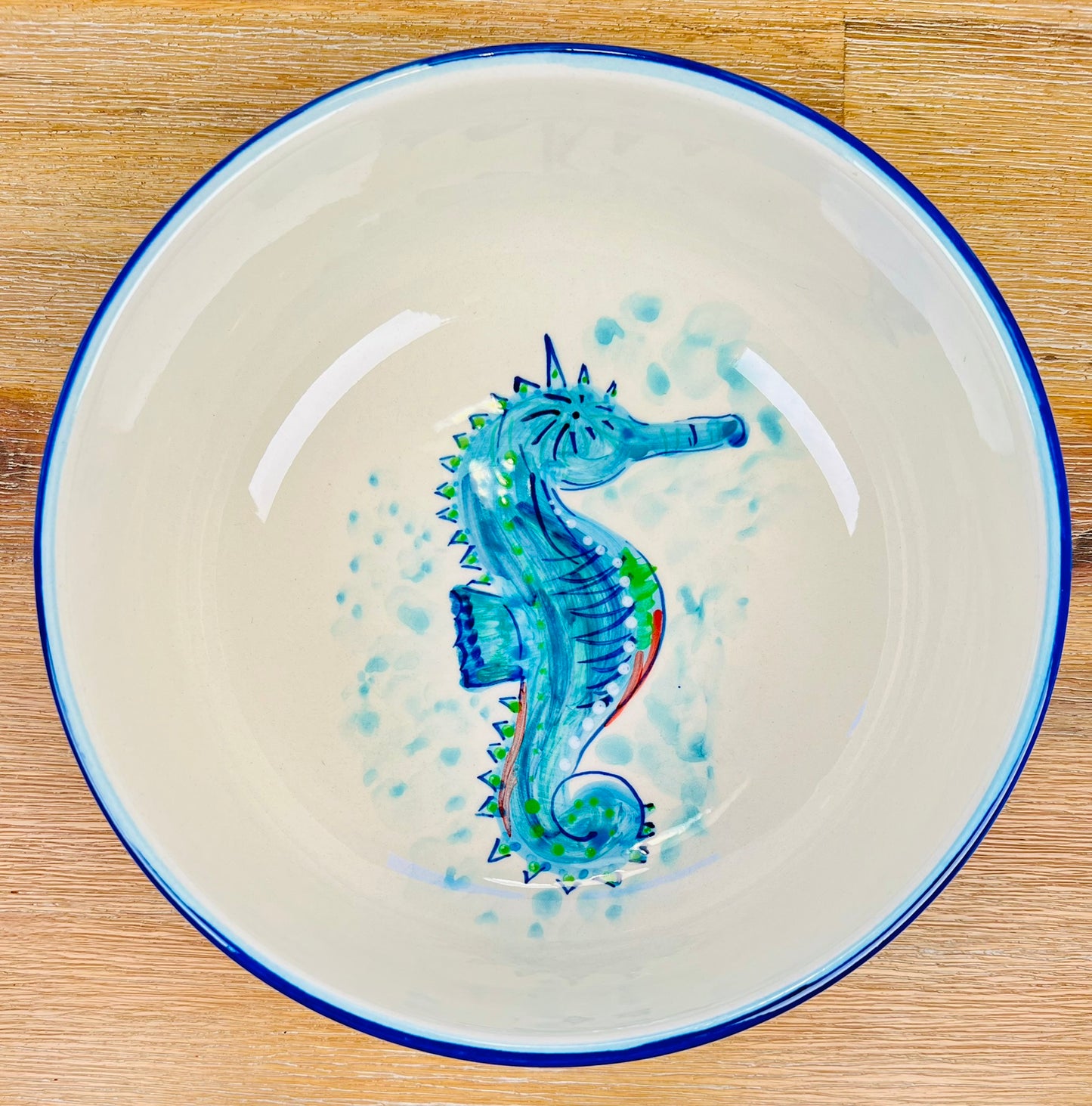 Handgemachte Keramikschale (23 cm) mit außen leuchtend blauer Glasur und handgemaltem Seepferdchen-Motiv in Blau-, Türkis- und Grüntönen, feinen Details und geschwungenen Linien auf weißem Grund.