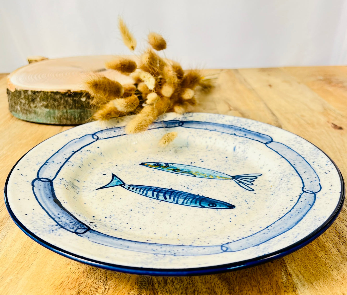 Handgemachter Keramikteller (25 cm) mit handgemaltem Motiv zweier stilisierter Sardinen in verschiedenen Blautönen auf cremeweißem Grund mit blauen Sprenkeln und kettenartigem, blauem Rand.