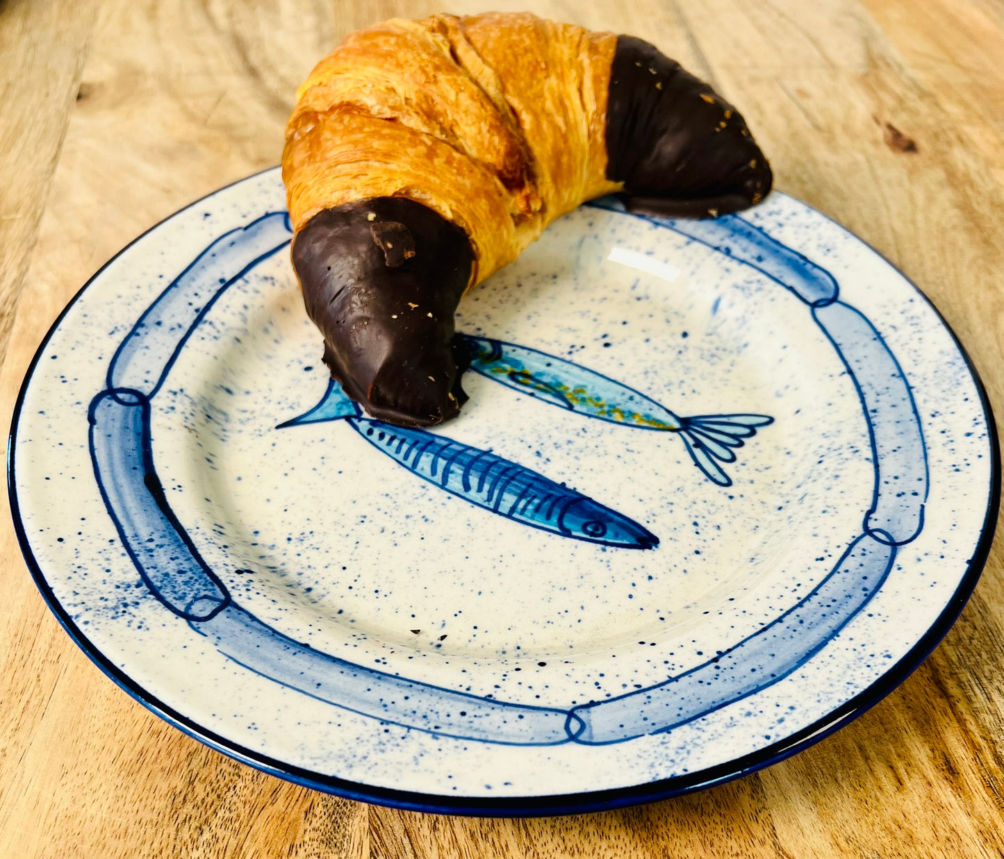 Handgemachter Keramikteller (25 cm) mit handgemaltem Motiv zweier stilisierter Sardinen in verschiedenen Blautönen auf cremeweißem Grund mit blauen Sprenkeln und kettenartigem, blauem Rand.
