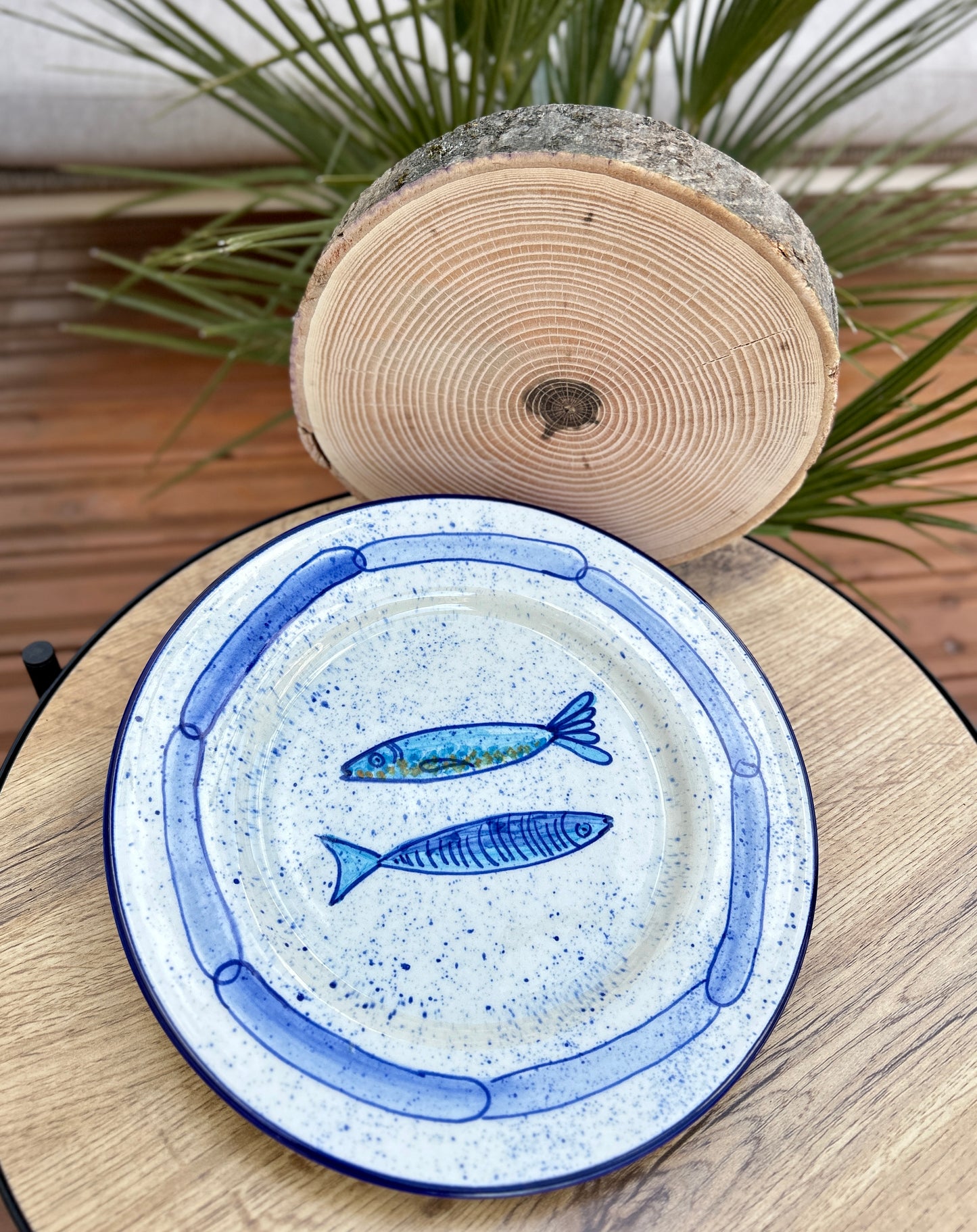 Handgemachter Keramikteller (25 cm) mit handgemaltem Motiv zweier stilisierter Sardinen in verschiedenen Blautönen auf cremeweißem Grund mit blauen Sprenkeln und kettenartigem, blauem Rand.