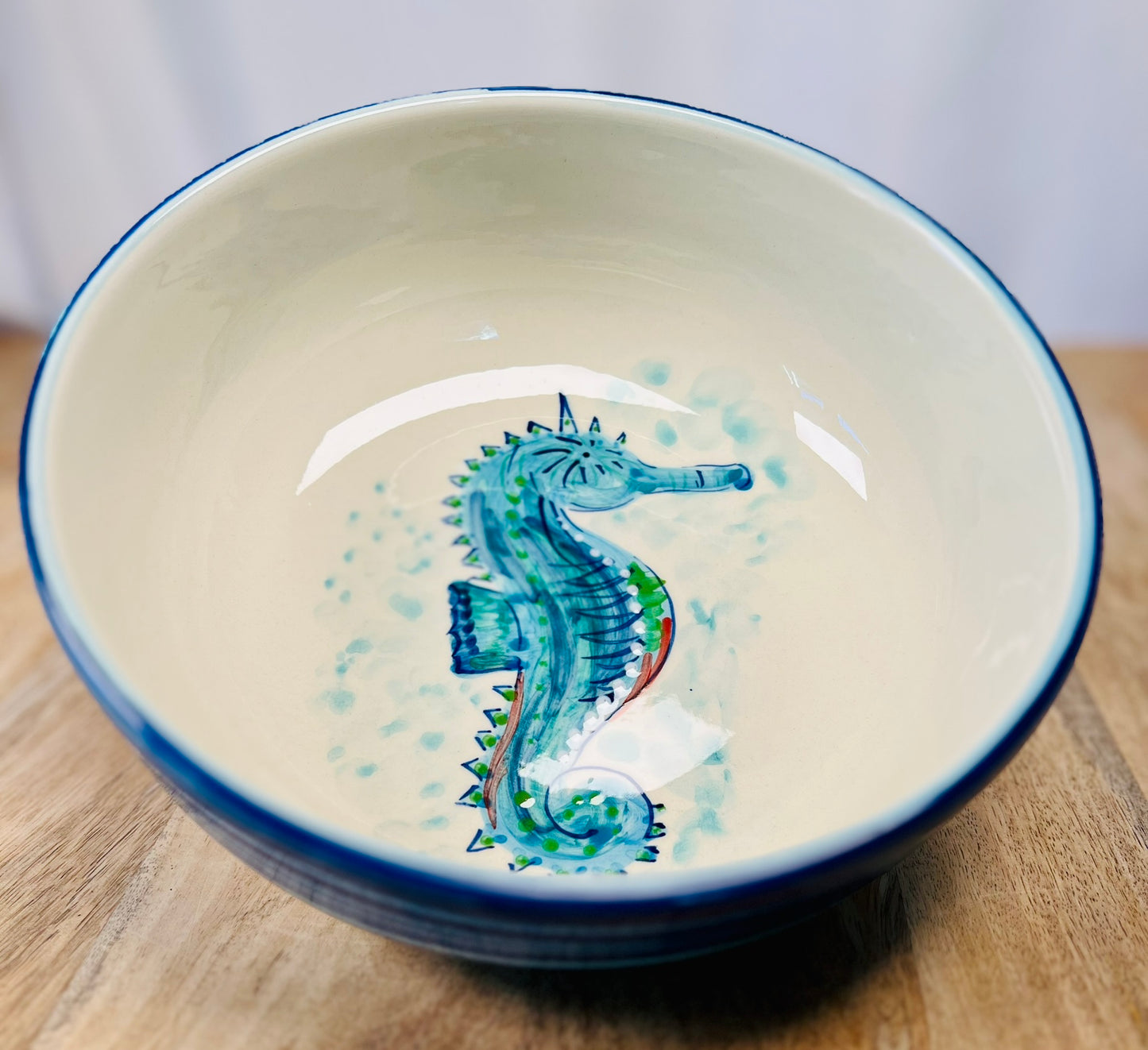 Handgemachte Keramikschale (23 cm) mit außen leuchtend blauer Glasur und handgemaltem Seepferdchen-Motiv in Blau-, Türkis- und Grüntönen, feinen Details und geschwungenen Linien auf weißem Grund.