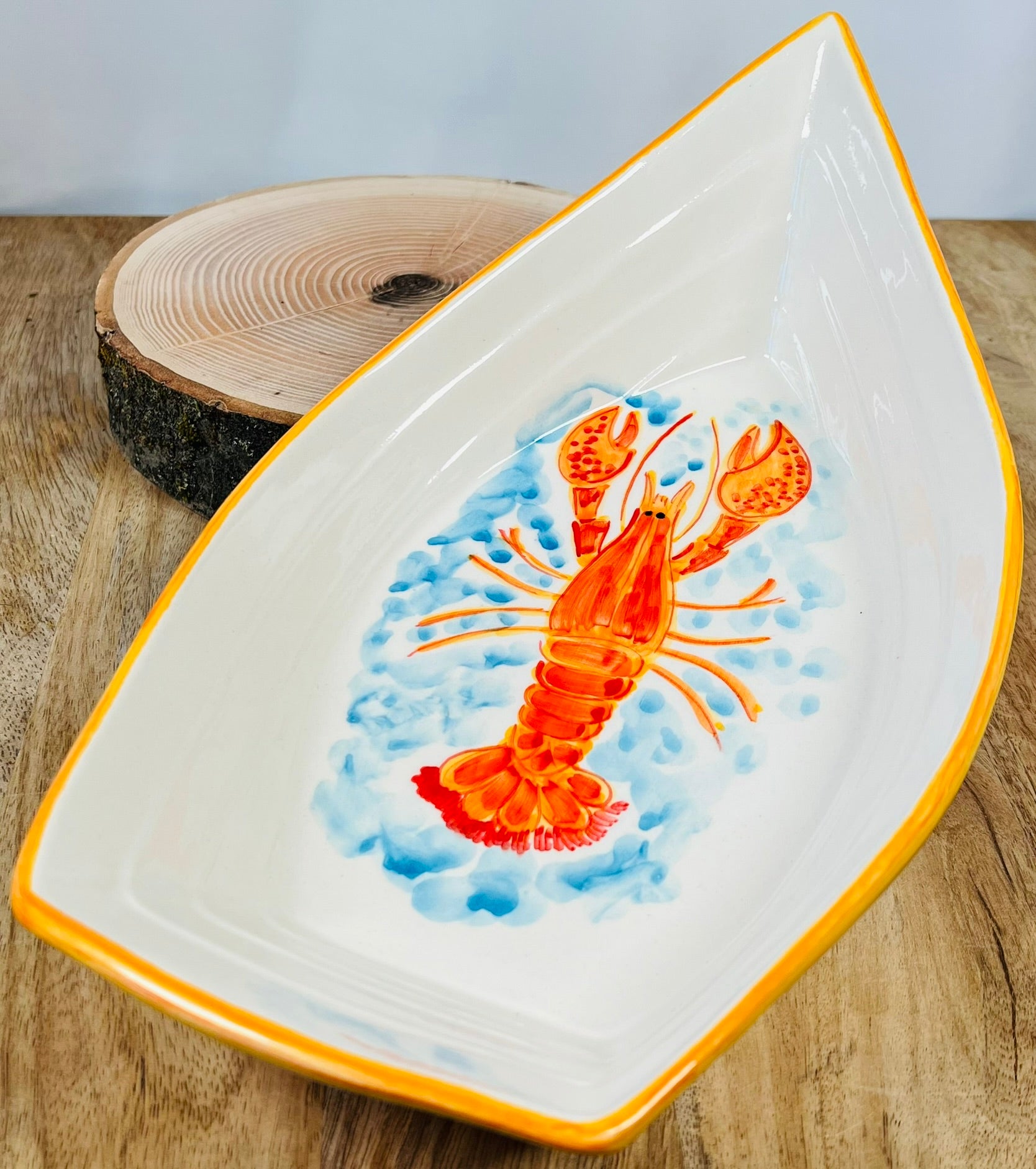 Handgemachte Keramikschale in kreativer Bootsform (34 cm) mit detailreich handgemaltem, leuchtend orangem Hummer-Motiv, geschwungenen Linien und zarten blauen Wasserakzenten auf weißem Grund.
