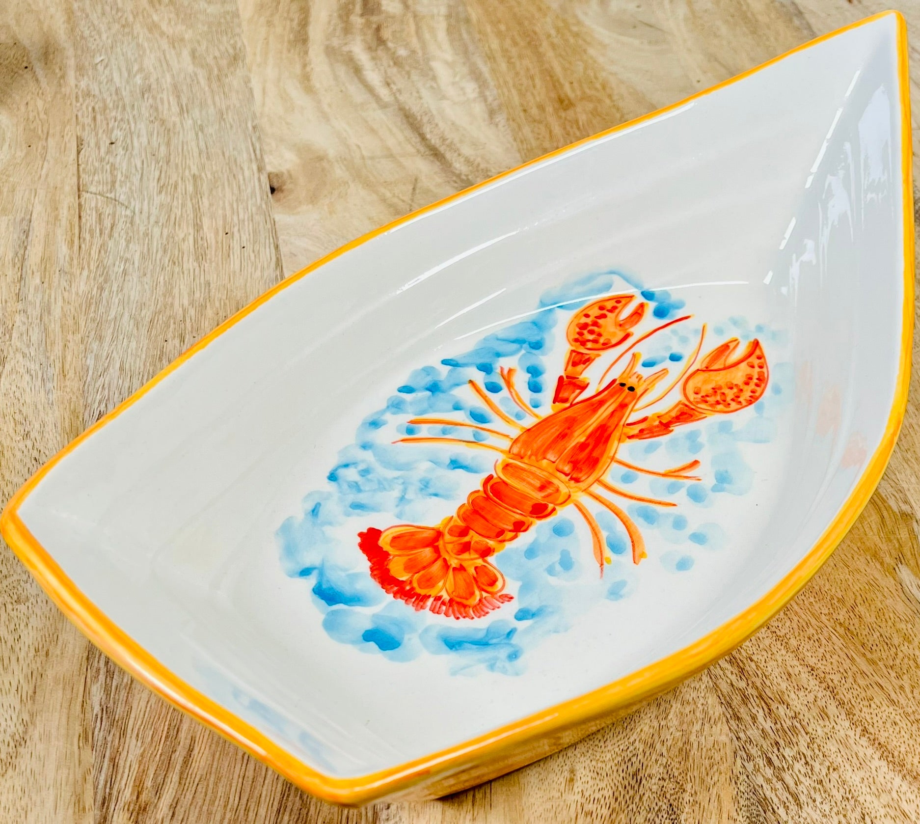 Handgemachte Keramikschale in kreativer Bootsform (34 cm) mit detailreich handgemaltem, leuchtend orangem Hummer-Motiv, geschwungenen Linien und zarten blauen Wasserakzenten auf weißem Grund.